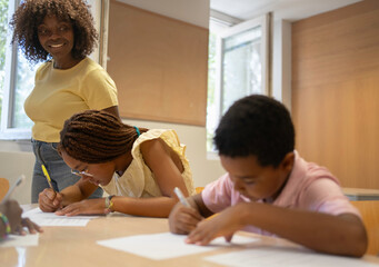 Fototapeta premium Happy african teacher watching students concentrating on their schoolwork at tables