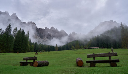 The mountain landscape of wild Friuli Dolomites, UNESCO Heritage. Nature reserves Dolomiti Friulane and Forra del Cellina. Mountain ranges. Mist shrouds a coniferous forest. A green lawn and benches. © A.Pushkin