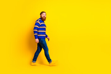 Stylish man in a striped sweater confidently walking against a yellow background conveying modern casual style