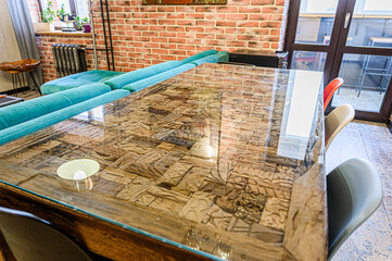 A modern interior showcases a unique wooden mosaic table with a glass top, complemented by colorful chairs and a turquoise sofa