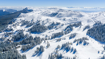 High-altitude drone shot showing the snow-covered peaks and ski lifts of Jahorina under bright blue sky