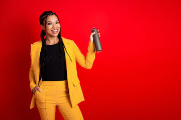 Young stylish woman in a yellow suit showcasing a spray can against a vibrant red backdrop, symbolizing creativity.