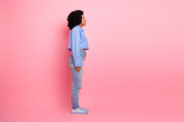 Young stylish woman in casual outfit against a pink background standing confidently