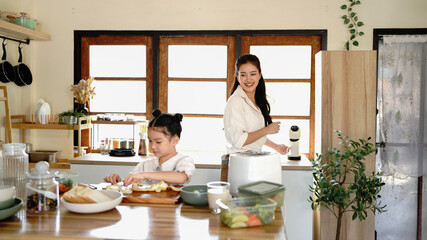 A mother and a child are in a kitchen, preparing food. The woman is smiling. The kitchen is well-equipped with various appliances and utensils