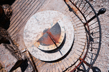 Aerial view of a weathered sundial with a rusty gnomon, surrounded by a metal railing on a stone platform.