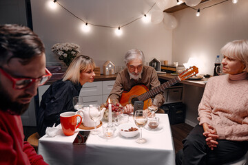 A group of people gather in a cozy room, sharing moments of joy, music, and fellowship during a casual meal. The scene is warmly lit and captures the essence of harmony and togetherness.