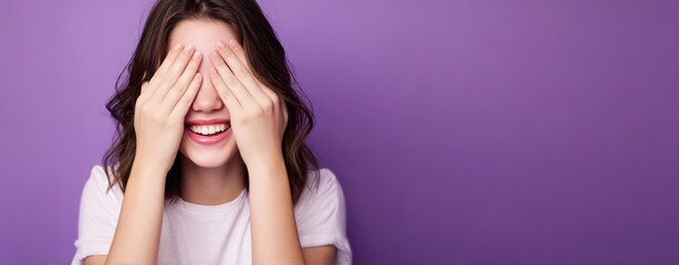 The woman covering her eyes and laughing against a purple studio background