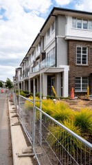 Suburban housing construction with temporary fencing, unfinished greenery, and modern design elements.