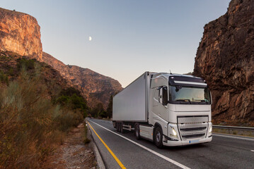 Refrigerated truck driving on a rural road between large mountains at sunset