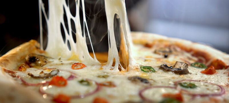 Hot pizza slice pulling a long strand of melted mozzarella cheese, creating a tempting gooey effect and showing appetizing fresh toppings, steam wafting from the crust