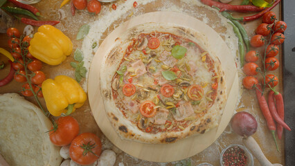 Delicious hot pizza on a wooden board, surrounded by fresh ingredients like bell peppers, tomatoes, mushrooms, basil, and red chili peppers on a rustic floured table, ready to be served