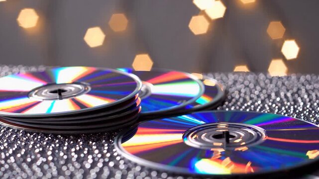 Shimmering CDs stacked on a textured surface create a colorful visual display with blurred lights in the background