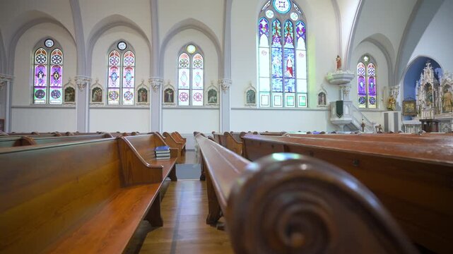 Moving along the aisle with wooden pews rows in empty church. Christian cathedral interior with wooden pews rows and white walls