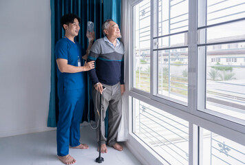 senior man patient leaning with cane,standing and relaxing by glass window,having infusion...