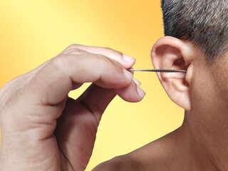 A man is putting ear pick metal, cleaning his ears for healthcare on a yellow background.