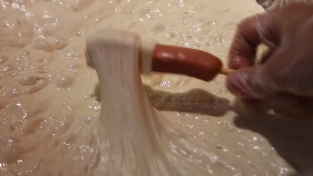 Close-up of a hotdog skewer dipped into thick batter, perfect for street food, corndog recipes, and snack preparation content.