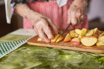 Elderly caucasian female slicing apples in kitchen with wooden cutting board and knife.