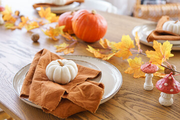 Autumn, fall, Halloween or thanksgiving day festive table setting. Fallen leaves, pumpkins and napkin on plate on wooden table background.