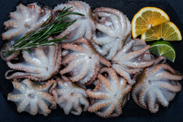 Fresh baby octopus, on black slate, with lemon and greenery, top view, no people,