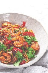 udon noodles, shrimp with vegetables and fresh herbs, in a bowl with chopsticks, light background, homemade, no people,