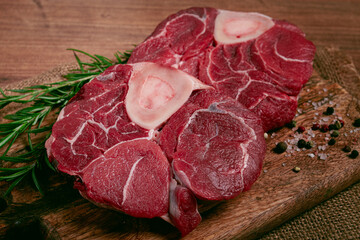 knuckle on the bone, raw meat for ossobuco, on a wooden chopping board, with a sprig of rosemary, and spices, top view, no people,