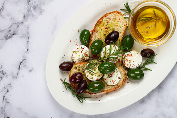 a plate with a snack, ciabatta bread with cheese and olives, olive oil, spices and herbs, top view, no people,