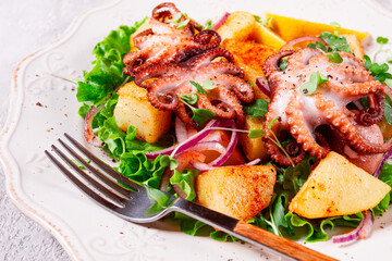Grilled octopus with baked potatoes and fresh herbs, on a decorative light plate, homemade, no people