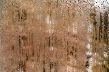 drops slowly sliding down wet window pane. Heavy condensation on apartment room window with thick water droplets obscuring view. brown backdoor. terracotta wet glass.