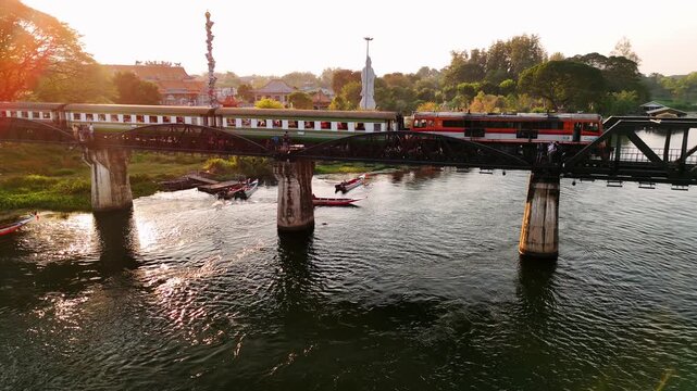 Train crossing famous river kwai bridge, death railway at golden sunset in kanchanaburi, thailand, showcasing cultural heritage moment.