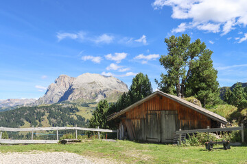 A lone wooden hut rests beneath towering peaks—Alpe di Siusi in quiet harmony