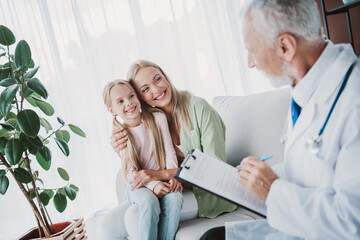Obraz premium A doctor meets a smiling mom and daughter during a friendly medical visit in a cozy living room setting and explains paperwork
