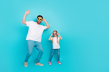 Single dad and daughter wearing colorful sunglass standing in teal background, enjoying time together, showcasing playful gestures