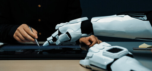 A human and robotic hand collaborate on a digital interface, showcasing the intersection of technology and creativity in a modern workspace environment.Noogenesis