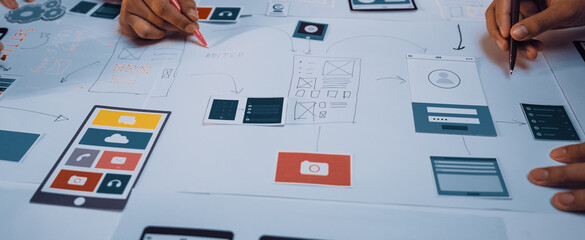 Hands of a creative team engage in collaboration around a table full of app design sketches and...