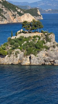 Close-up of rocky island fortress in Parga Greece. Surrounded by Ionian Sea and mountains, with trees on top of medieval ruins. Famous Greek coastal landscape and travel landmark.