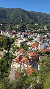 Traditional town houses with red roofs in Parga Greece. Mountain background and green hills surround Ionian coastal settlement. Authentic Greek town architecture and travel view.