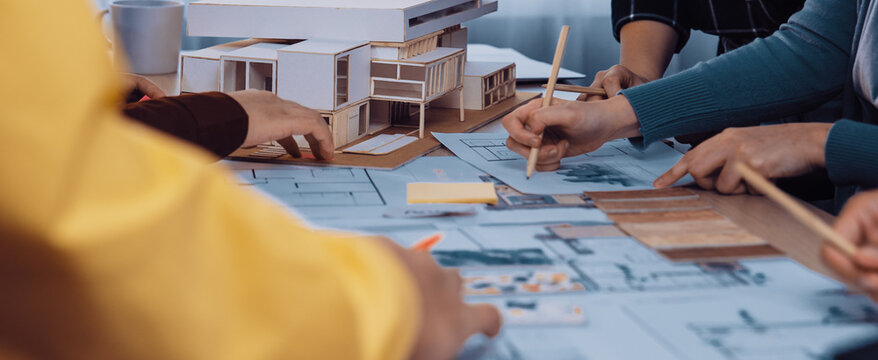 A group of architects collaborates on a building project, discussing blueprints and examining a detailed model. The scene captures creativity and teamwork in a modern workspace. SACTR