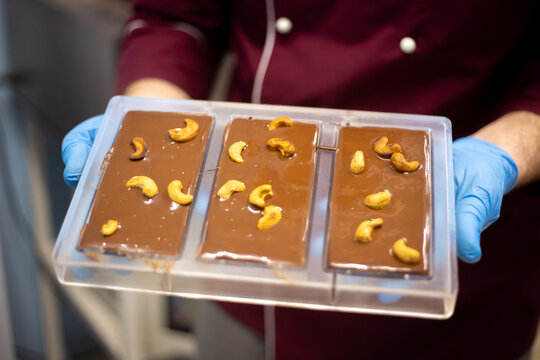 Close-up of a man holding a handcrafted bar of chocolate made at home with crunchy cashews,