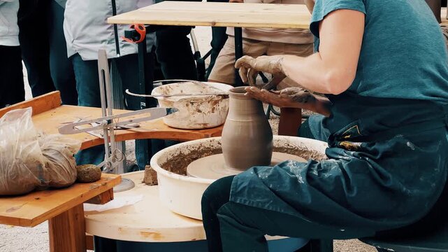 A female potter shaping clay on a pottery wheel during a public workshop at a local artisanal fair, demonstrating handmade ceramics process and pottery techniques