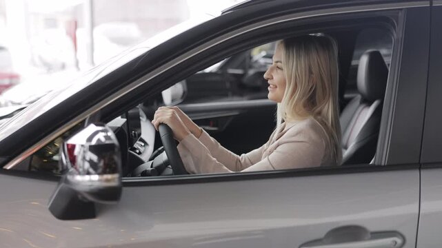 Happy business woman sitting in new car at dealership showroom