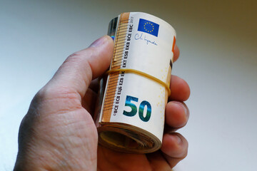 A man's hand holding a roll of 1,000 euros in 50-euro bills. Stack of Europe money. Stack of euro money. Stack of 50 euros isolated on white background. Concept of savings, salary, pension or mortgage