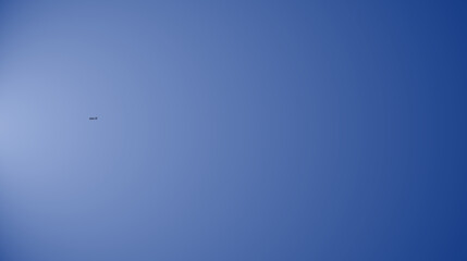 Fototapeta premium Distant airplane soaring through a vast clear blue sky