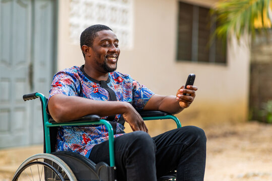 African man in wheelchair using mobile phone for mobile money transaction outdoors - Powered by Adobe