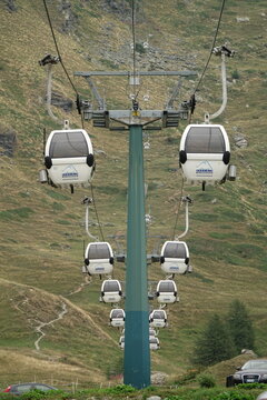 Multiple white gondolas hang from cables on a ski lift structure amidst grassy slopes in summer time in the Breuil-Cervinia, Valtournenche, Aosta Valley, Italy
