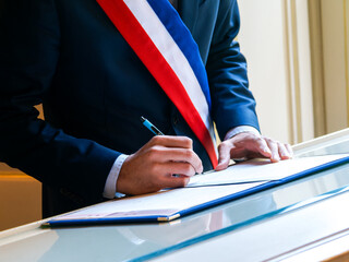 Signature officielle d’un acte de mariage civil par un élu portant l’écharpe tricolore française, symbole de la République et de l’union légale