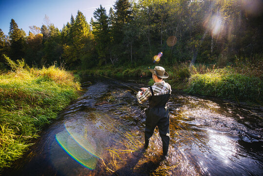 A man in fishing vader stands in the river and catches fish on a spinning rod.