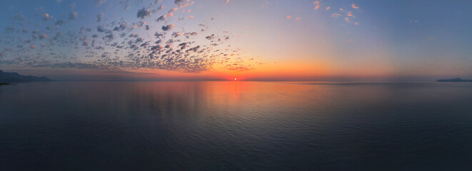 A tranquil shot of a stunning sunrise over calm sea waters, with a peaceful horizon and subtle clouds reflecting warm golden tones. Antalya, Turkey