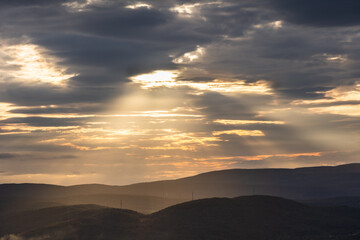 A landscape with sunbeams over rolling hills.