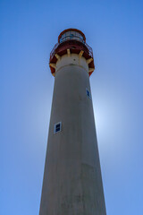 Bright sunny day shines behind tall lighthouse standing proudly against clear blue sky at coastal location during daytime
