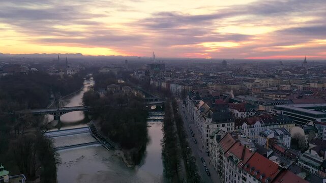4K Drohnenflug &uuml;ber die Isar in M&uuml;nchen bei Sonnenuntergang mit Alpenpanorama und Skyline mit Deutschem Museum, M&uuml;llerschem Volksbad, Gasteig, Maximilianbr&uuml;cke und Alter Peter.